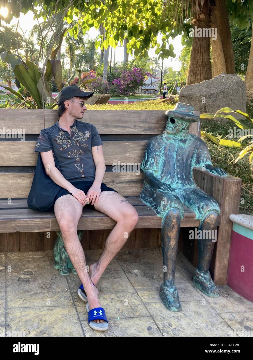 Man looks at brass statue on a bench. - Smartphone Captured Stock Image