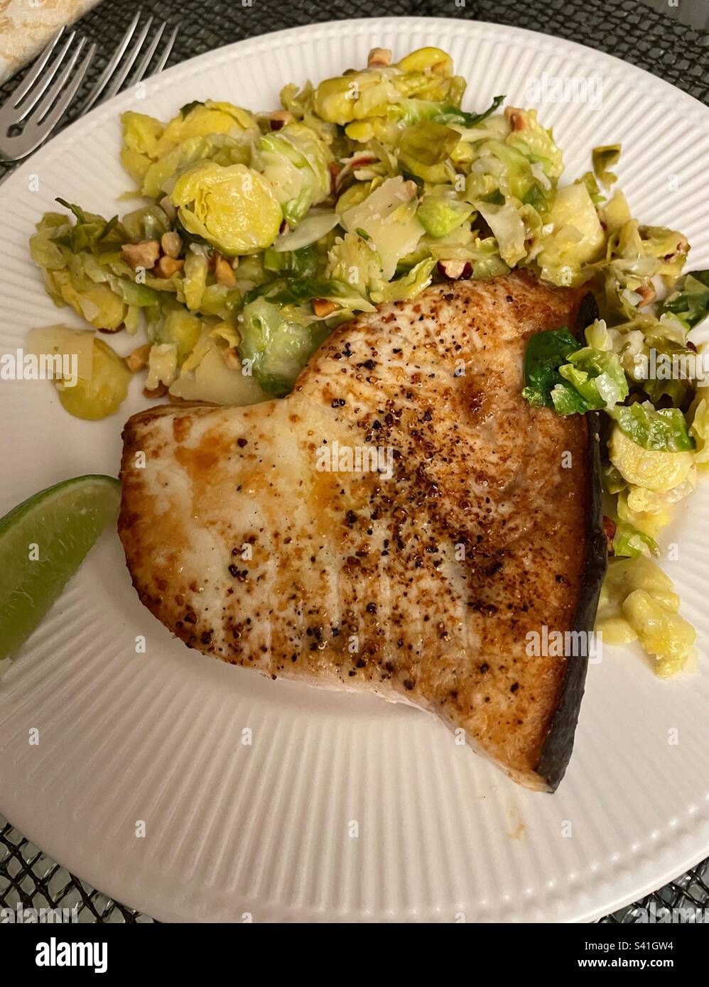 Close up of a gourmet meal of broiled swordfish and shaved Brussels sprouts on a white china plate, 2023, USA - Smartphone Captured Stock Image