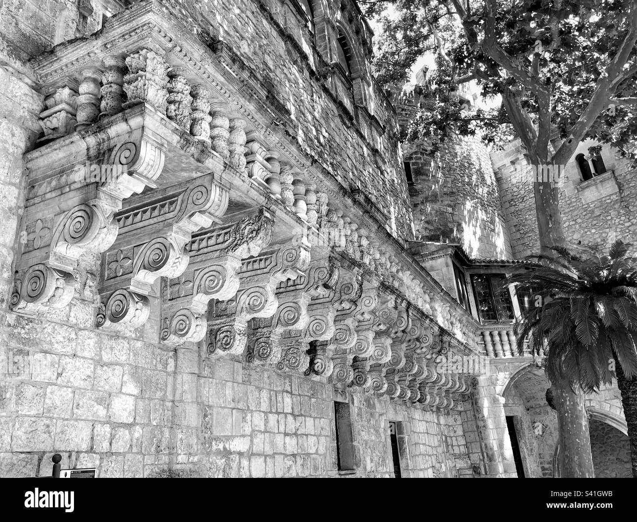 Black and white monochrome old building facade exterior architecture with long balconette and curl pattern support blocks - Smartphone Captured Stock Image