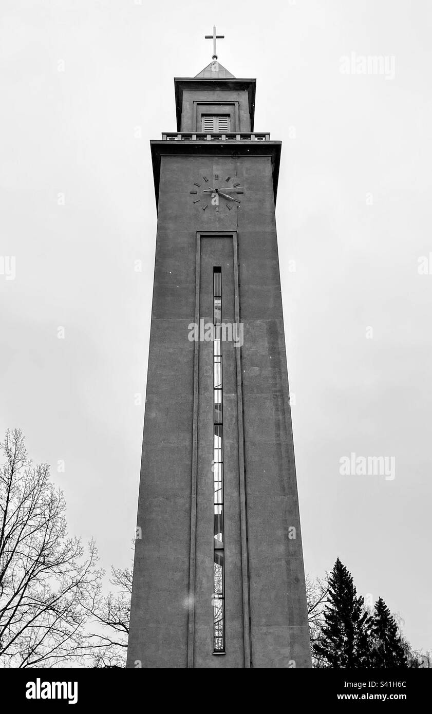 Black and white monochrome photo cemetery blessing chappel high and narrow building with clock and christian catholic cross against the sky - Smartphone Captured Stock Image