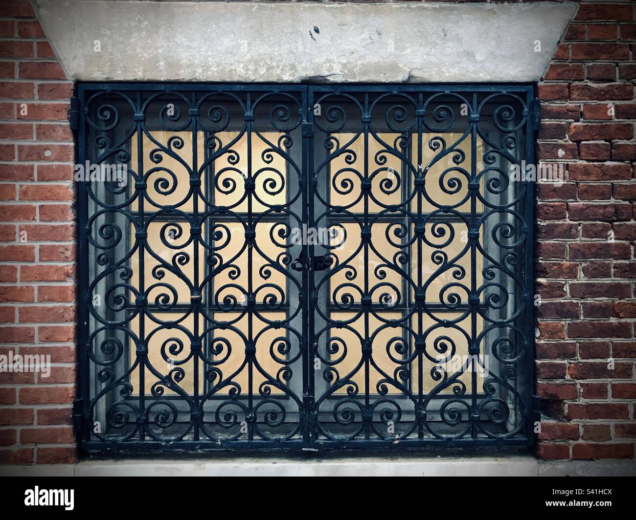 Backlit windows of an apartment, ornately blocked with iron scroll design for protection, at ground level on a street in Philadelphia - Smartphone Captured Stock Image