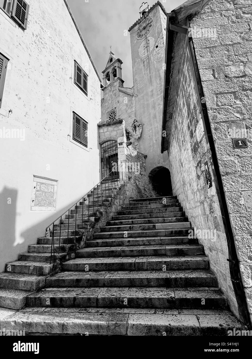 Black and white monochrome photo of the staircase between two old building walls with arcs and clock bells tower above - Smartphone Captured Stock Image