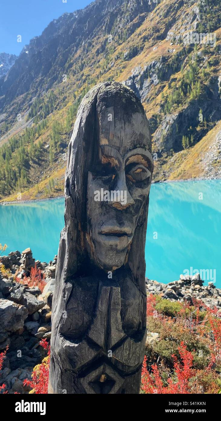 A wooden idol stands in the mountains against the backdrop of a high-altitude turquoise lake. - Smartphone Captured Stock Image
