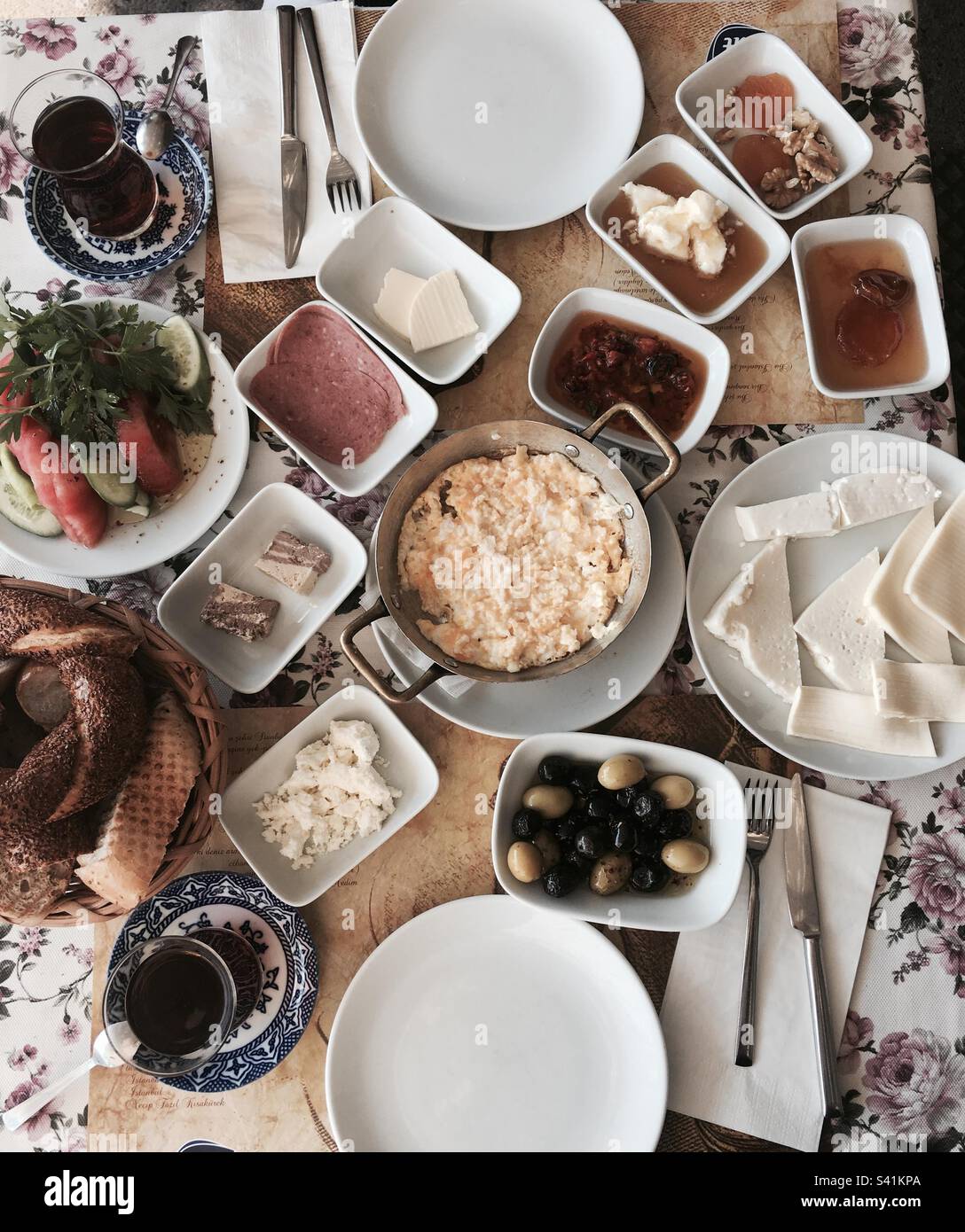 Turkish breakfast including scrambled eggs, olives, salami, cheese, honey  & cream, simit, jam, Turkish tea, bread, halva, tomato, cucumber, parsley,butter, cutlery and two plates in Galata Istanbul - Smartphone Captured Stock Image