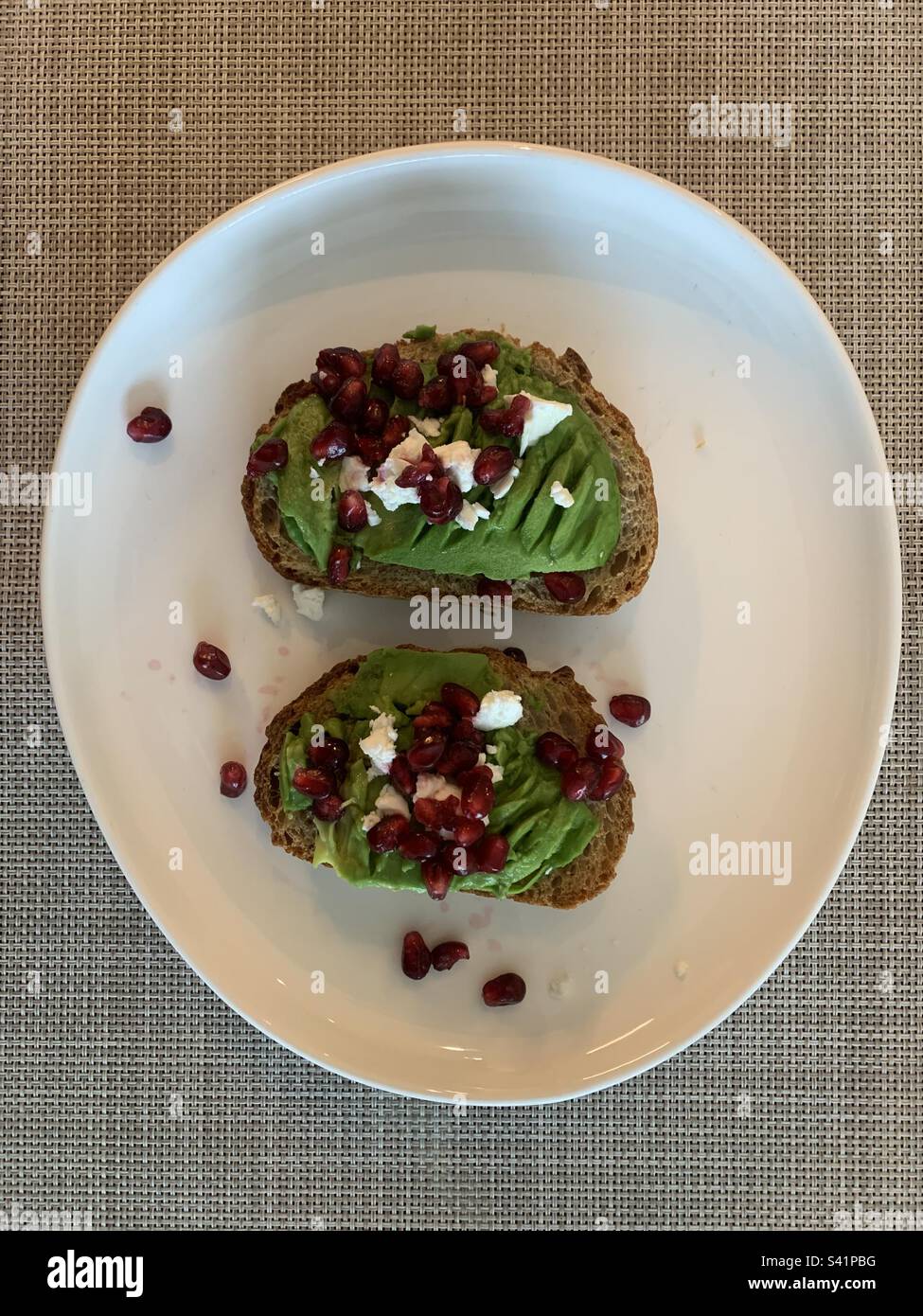 A slice of toasted sourdough bread topped with avocado, feta and pomegranate - Smartphone Captured Stock Image