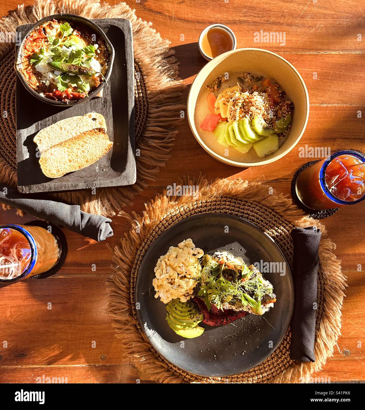 Healthy breakfast with scrambled eggs, avocado toast, fruits and yogurt, shakshouka, ice coffee with bohemian cutlery and utensils - Smartphone Captured Stock Image