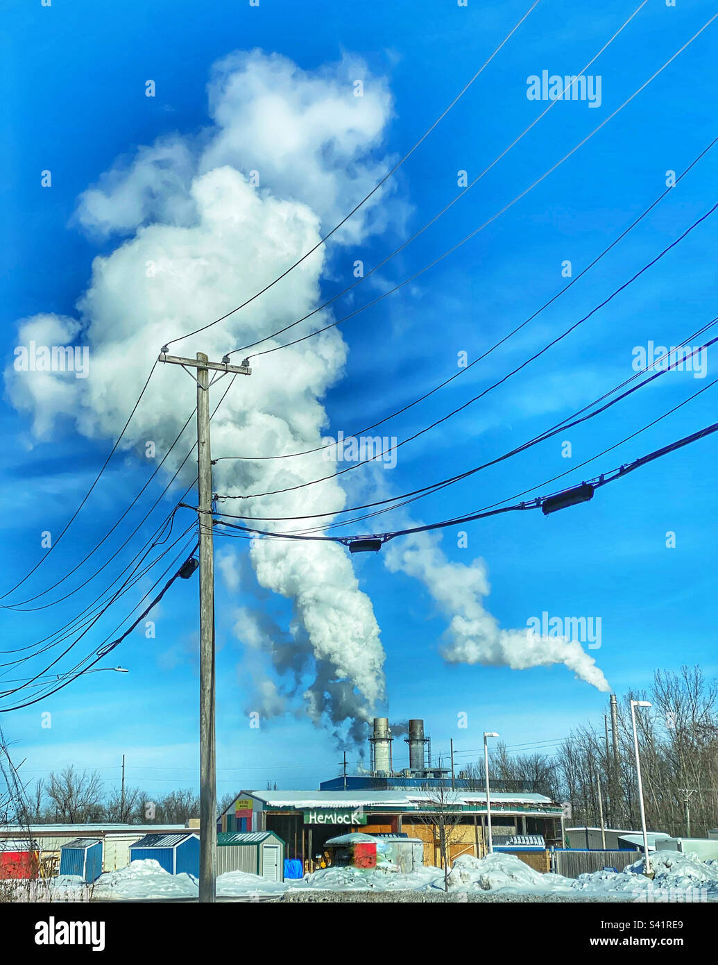 Hemlock sign on a building in front of a power plant with smoke rising from smokestacks Stock Photo