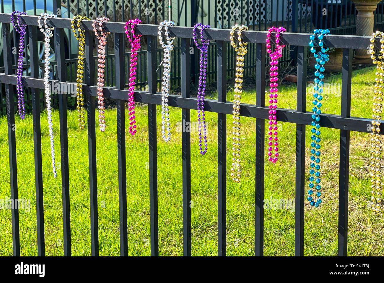Pretty multi coloured beads hanging from a garden fence to celebrate a Mardi Gras festival. No people. - Smartphone Captured Stock Image