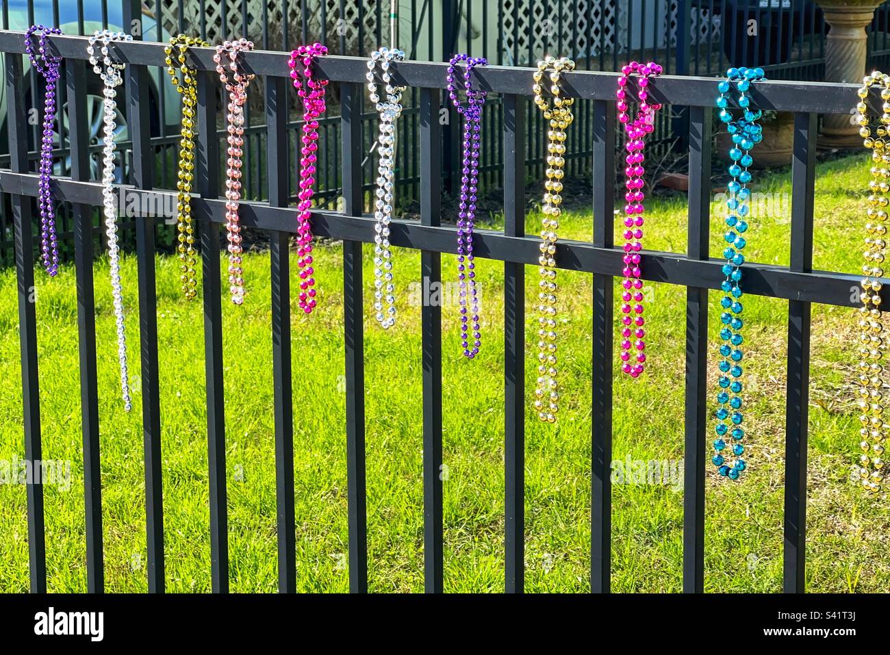 Pretty multi coloured beads hanging from a garden fence to celebrate a Mardi Gras festival. No people. Stock Photo