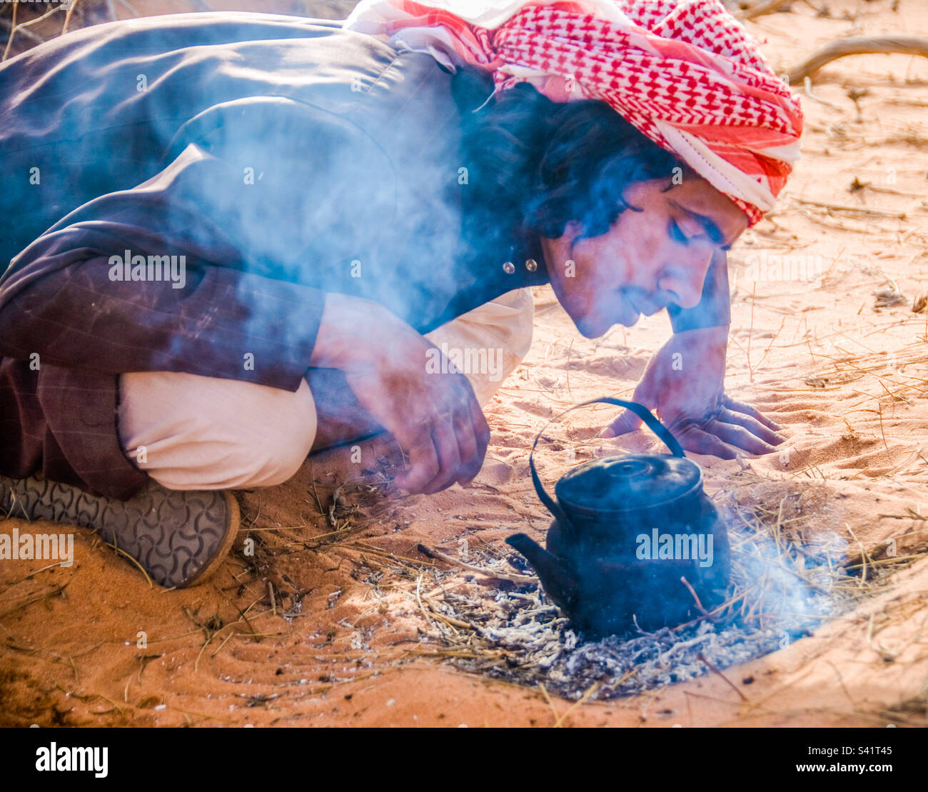 A tour guide makes tea for his clients over a small fire in the desert - Smartphone Captured Stock Image