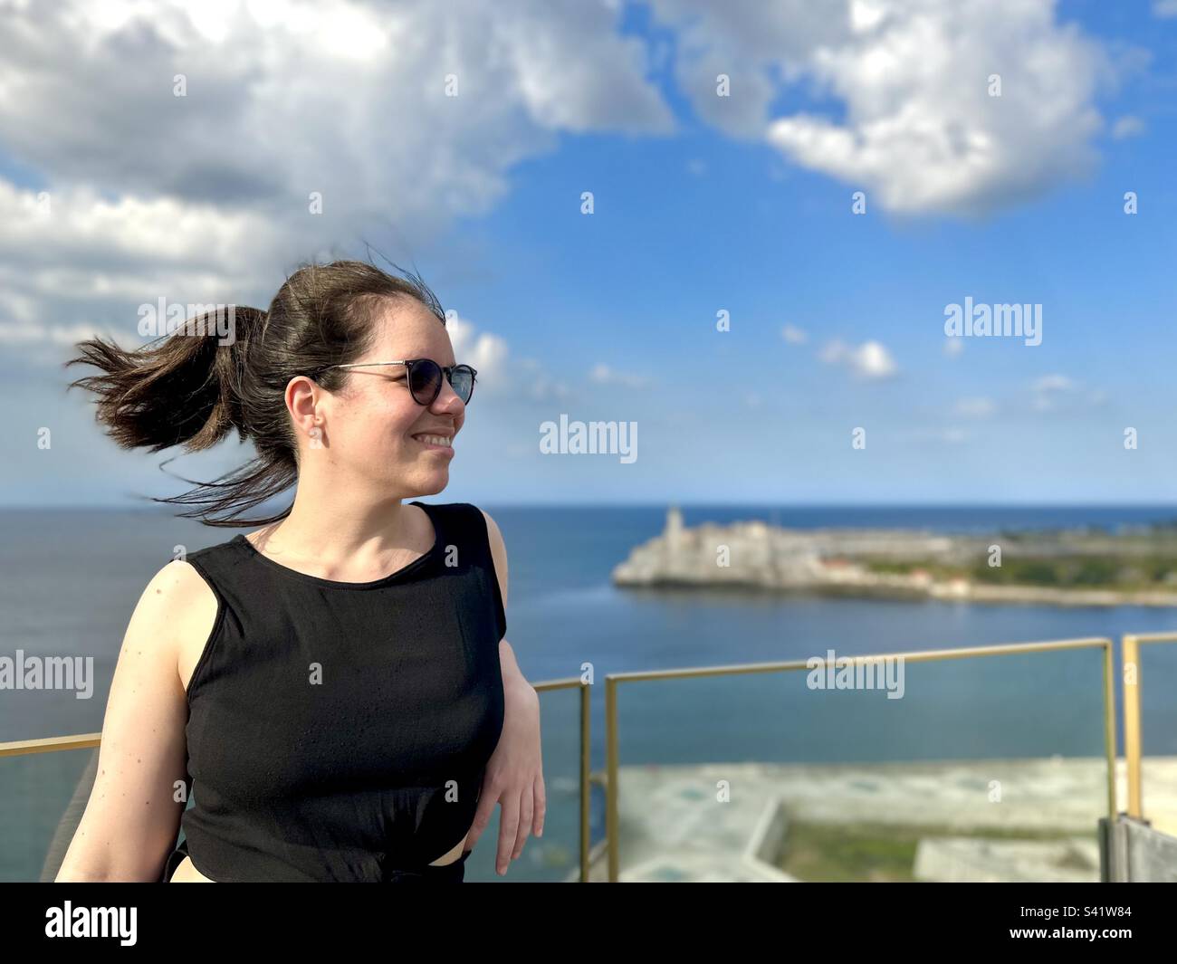 Woman looking away. Havana’s lighthouse blurred in the background. El Morro, Cuba - Smartphone Captured Stock Image