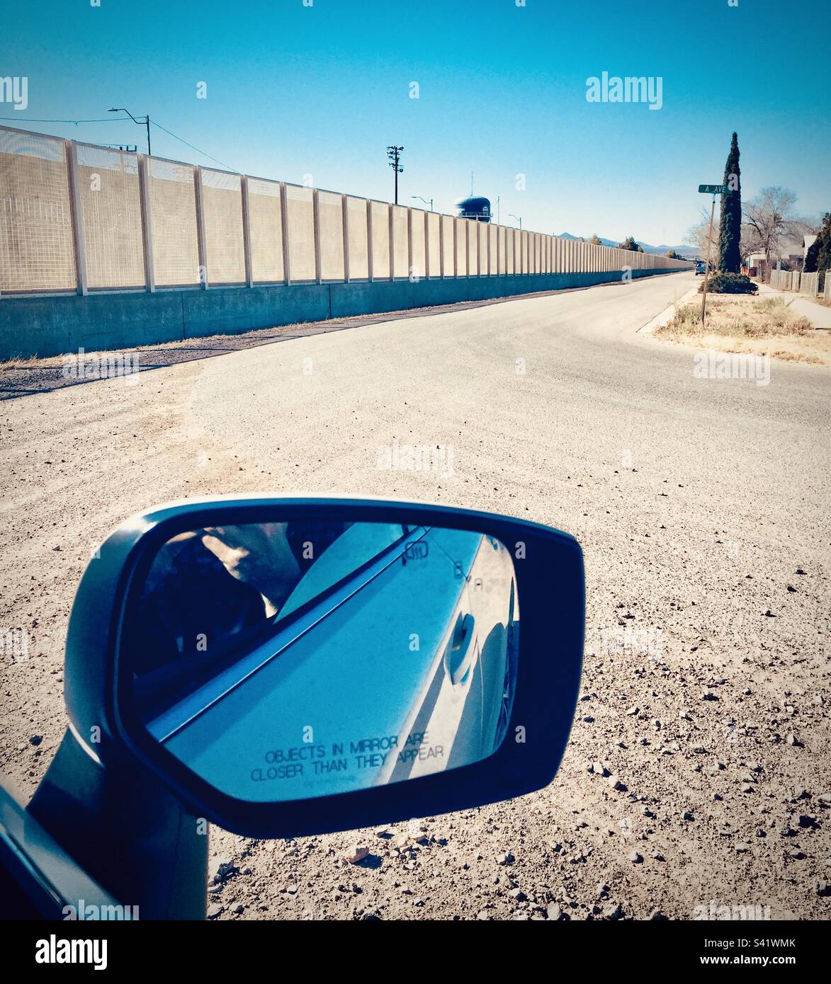 A car wing mirror in the foreground with the USA Mexico border wall in the background in Texas - Smartphone Captured Stock Image