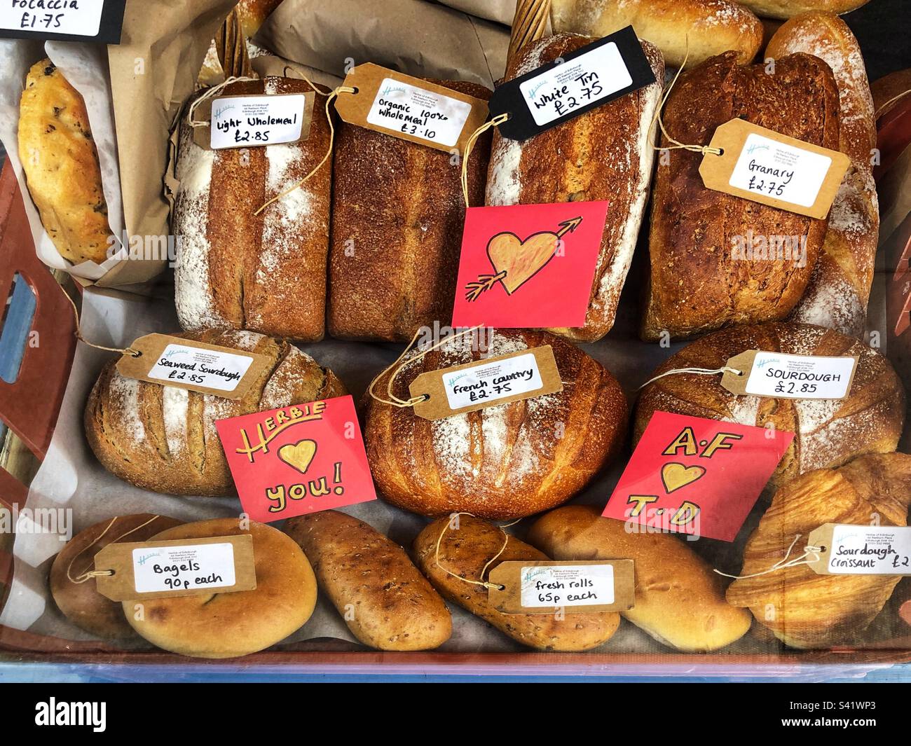 Fresh artisan crusty bread loaves with price tags in a speciality delicatessen and charcuterie shop window display just before Valentine’s Day Stock Photo