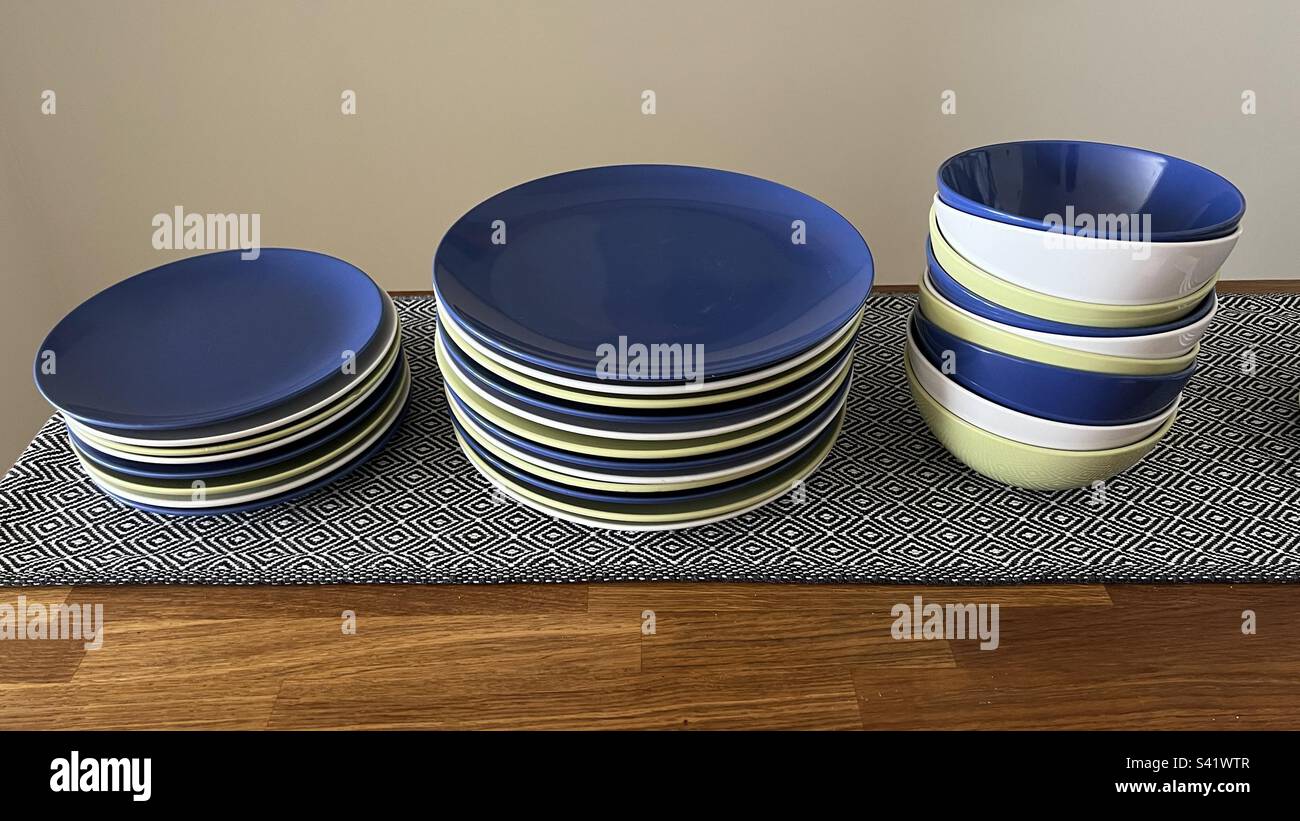 Set of blue, green, and white ceramic plates, dinner plates, and bowls on a wooden table with patterned cloth - Smartphone Captured Stock Image