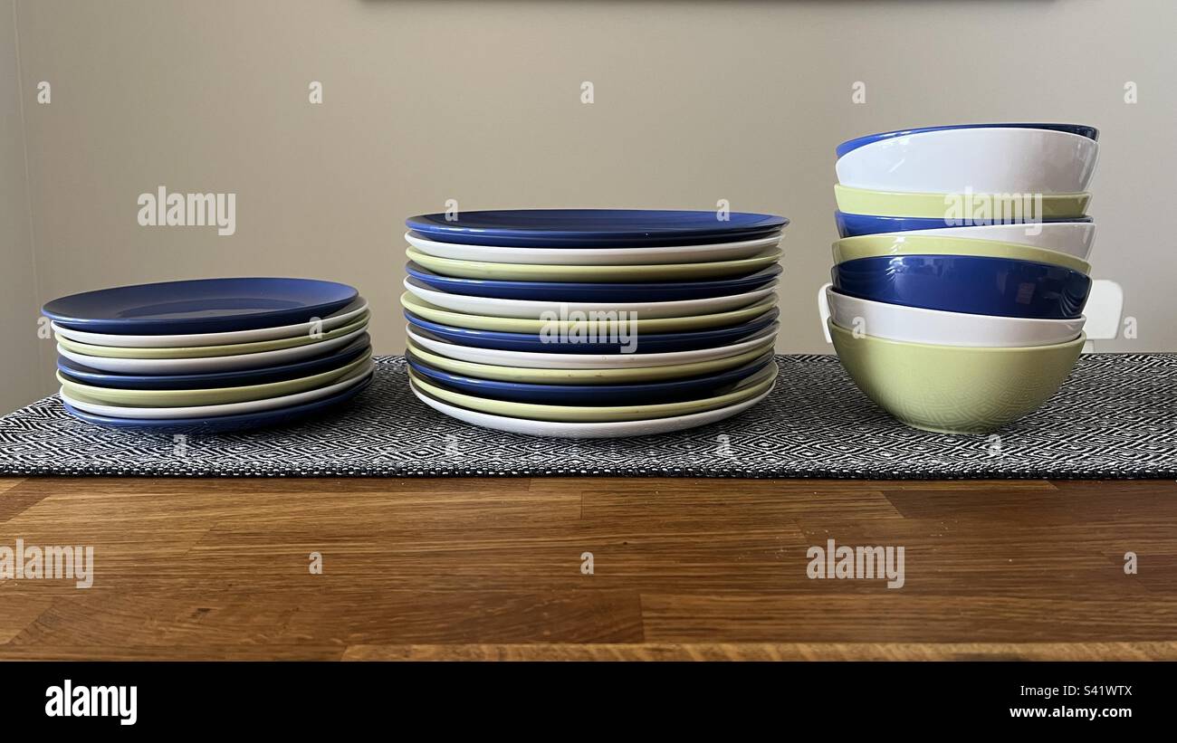 Side view of blue, green, and white ceramic plates, dinner plates, and bowls on a wooden table with patterned cloth - Smartphone Captured Stock Image