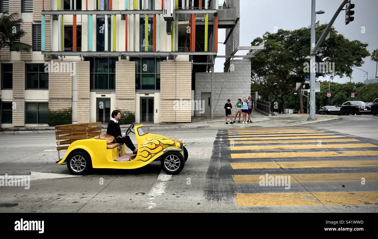 SANTA MONICA, CA, AUG 2022: woman driving a distinctive, bright yellow, custom car, stopped at yellow crosswalk next to modern apartment building - Smartphone Captured Stock Image
