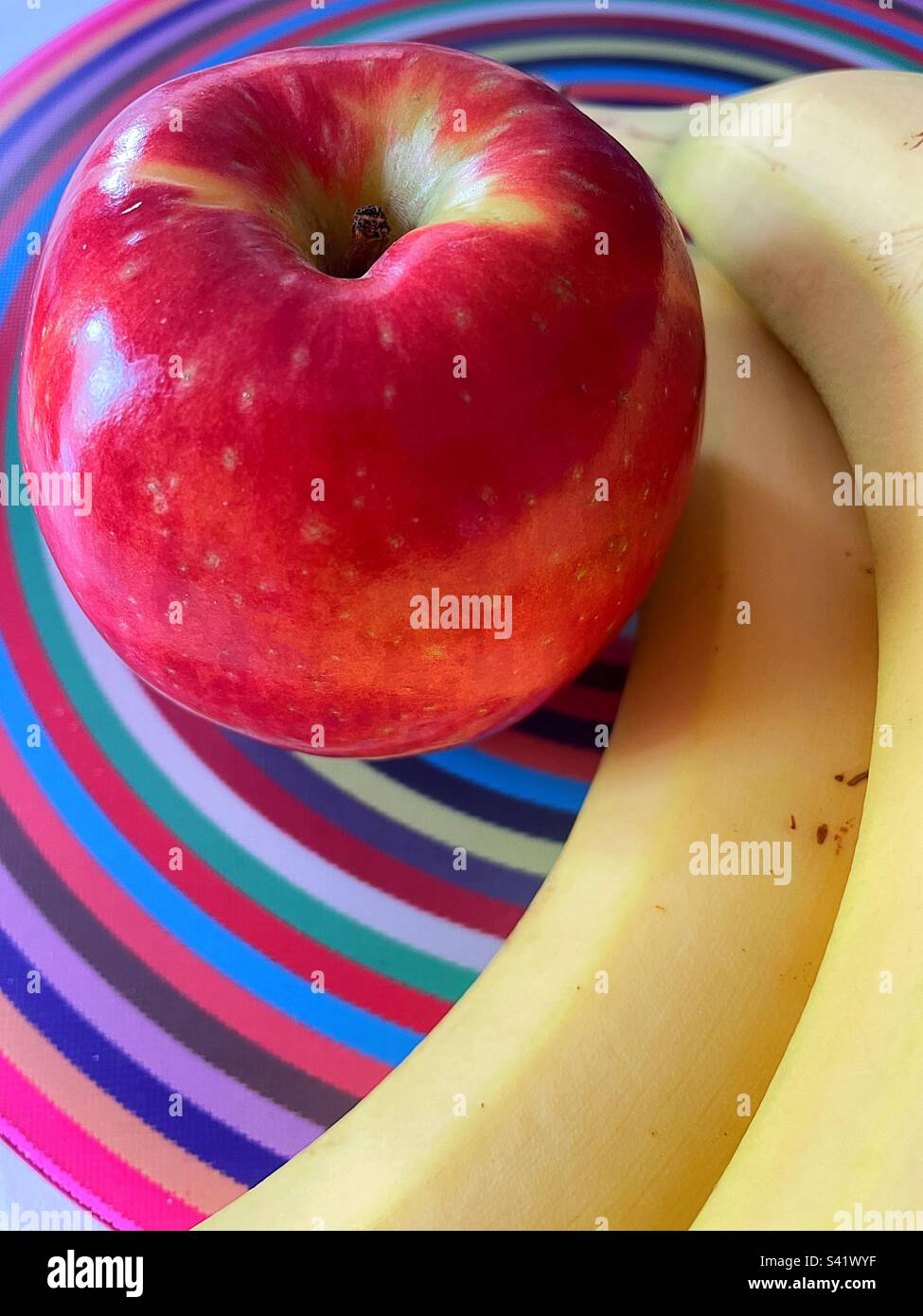 Close up of a fresh apple and bananas on a multi colored cutting board, 2023, USA - Smartphone Captured Stock Image