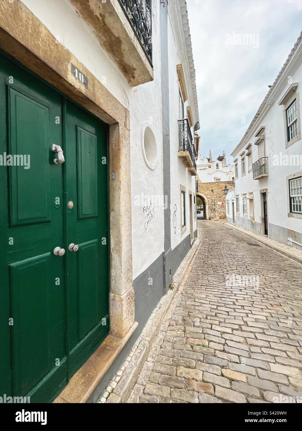 Old cobbled street leading to the ancient city wall of Faro - door with an interesting knocker - Arco da Vila in distance. Portugal’s history. - Smartphone Captured Stock Image