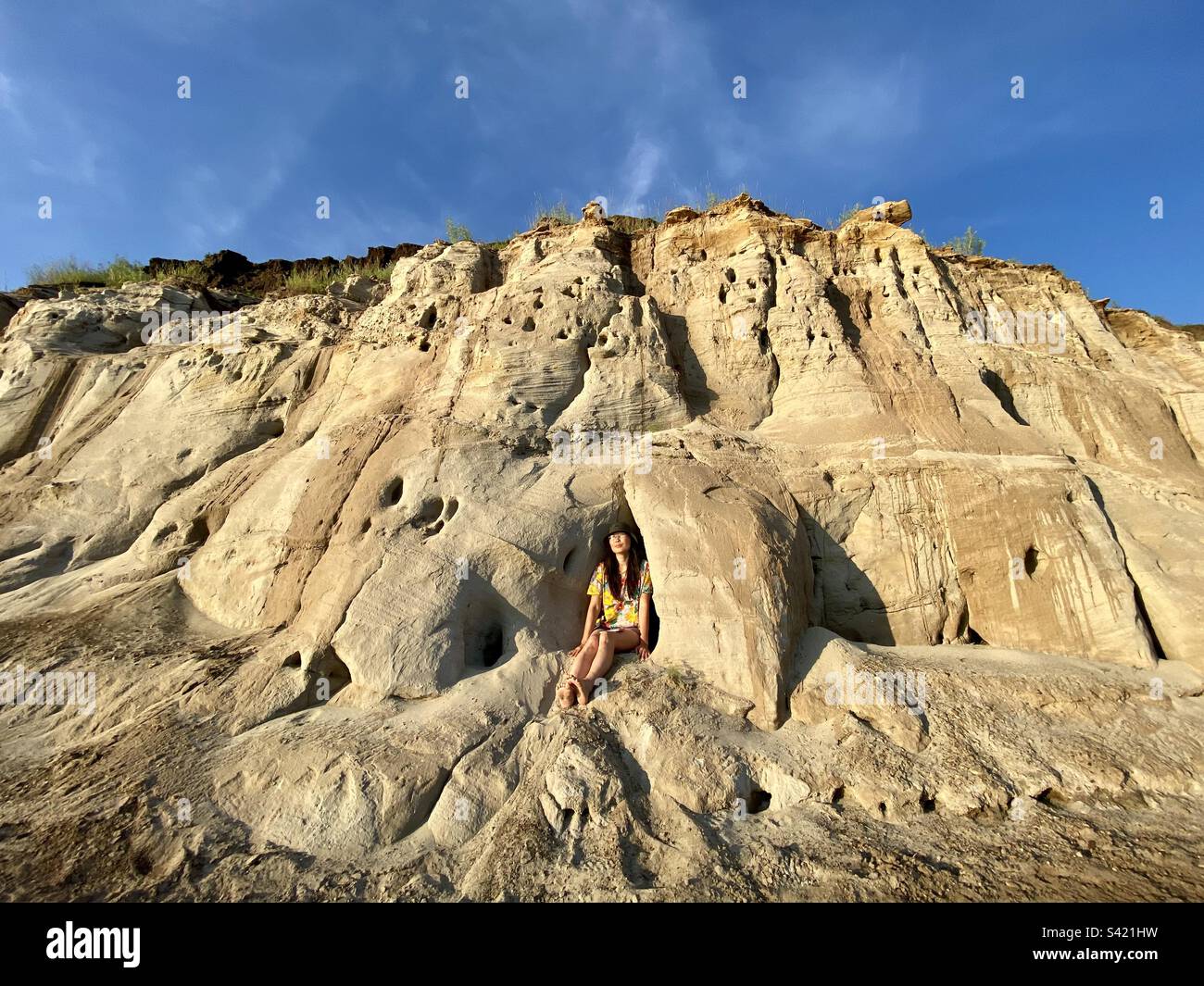 A Yakut girl in shorts sits at a clay cave near an erosive sandy relief form of mountains in Yakutia Stock Photo