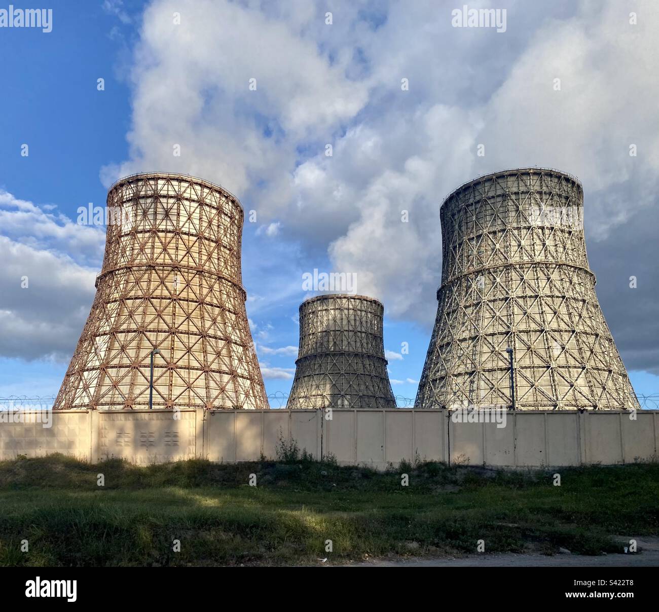 The big pipes of the coal-fired thermal power plant stand and smoke behind the fence against the sky. Stock Photo