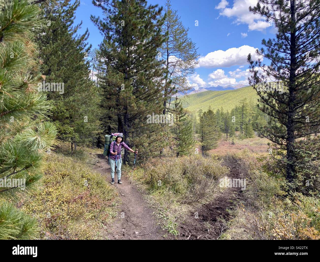 An Asian girl traveler Yakut stands with a backpack on a trail in the Altai mountains in Siberia. Stock Photo