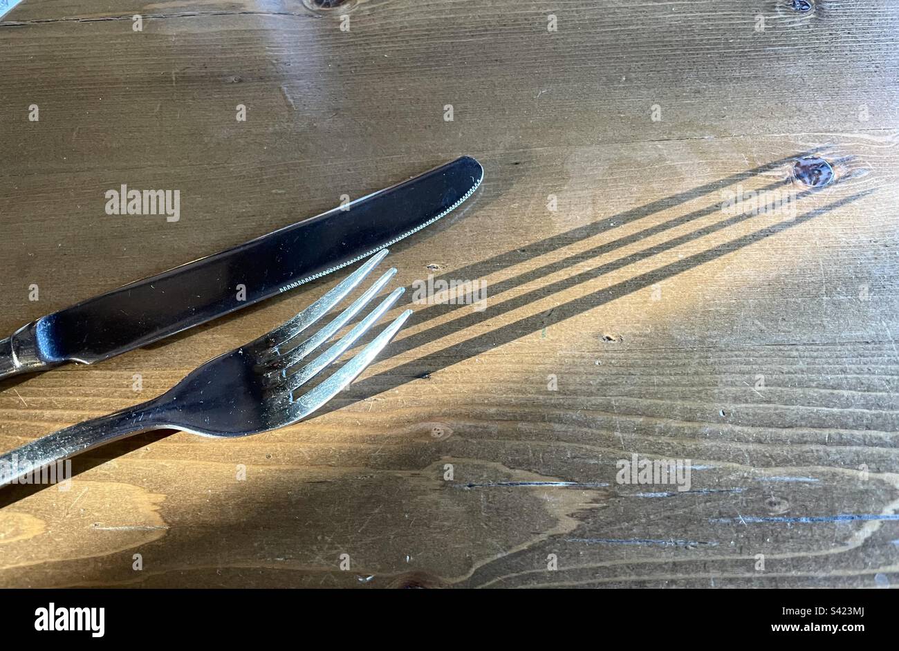 Long shadow of a dinner fork on a wood dining table’s - Smartphone Captured Stock Image