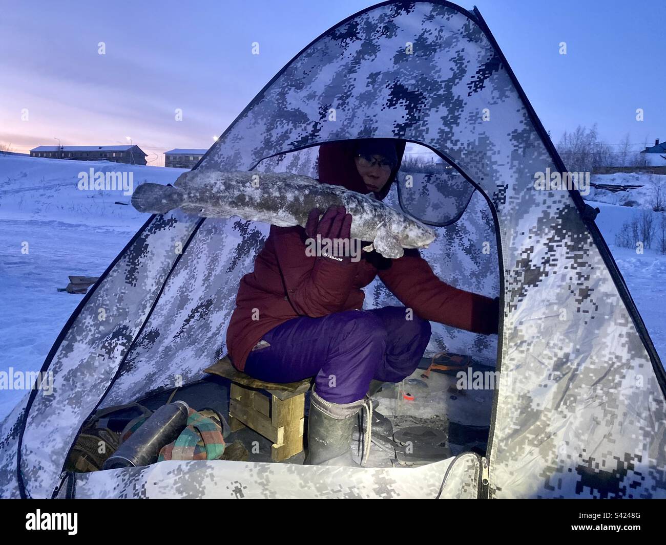 A Yakut girl is fishing in a tent in winter in the cold with snow in the village of Yakutia. Stock Photo