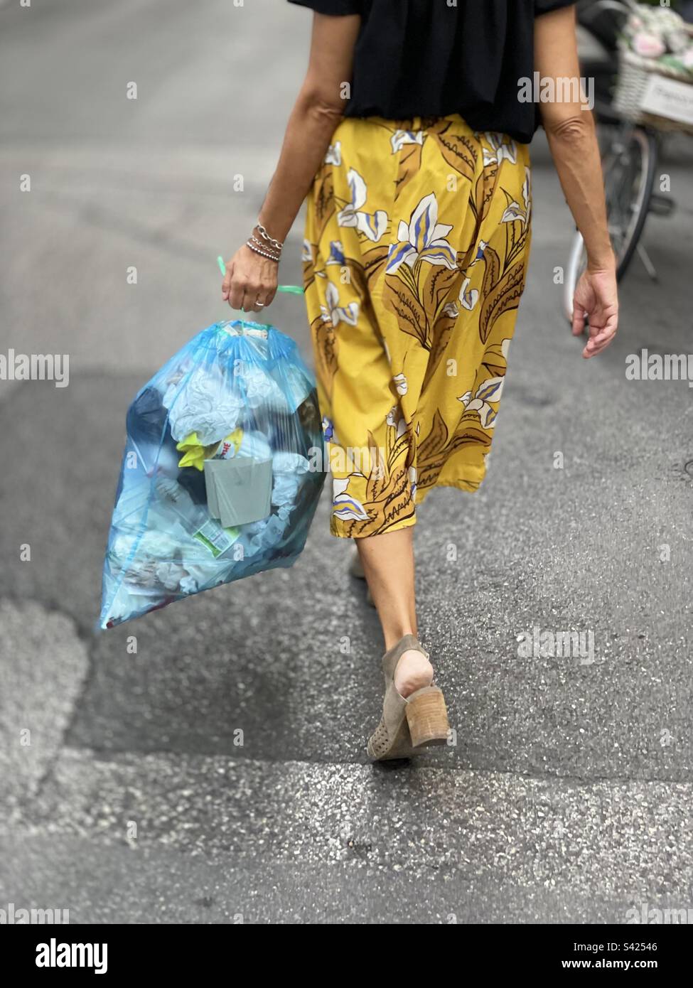 Woman from behind walking taking the trash out in plastic bag Stock Photo