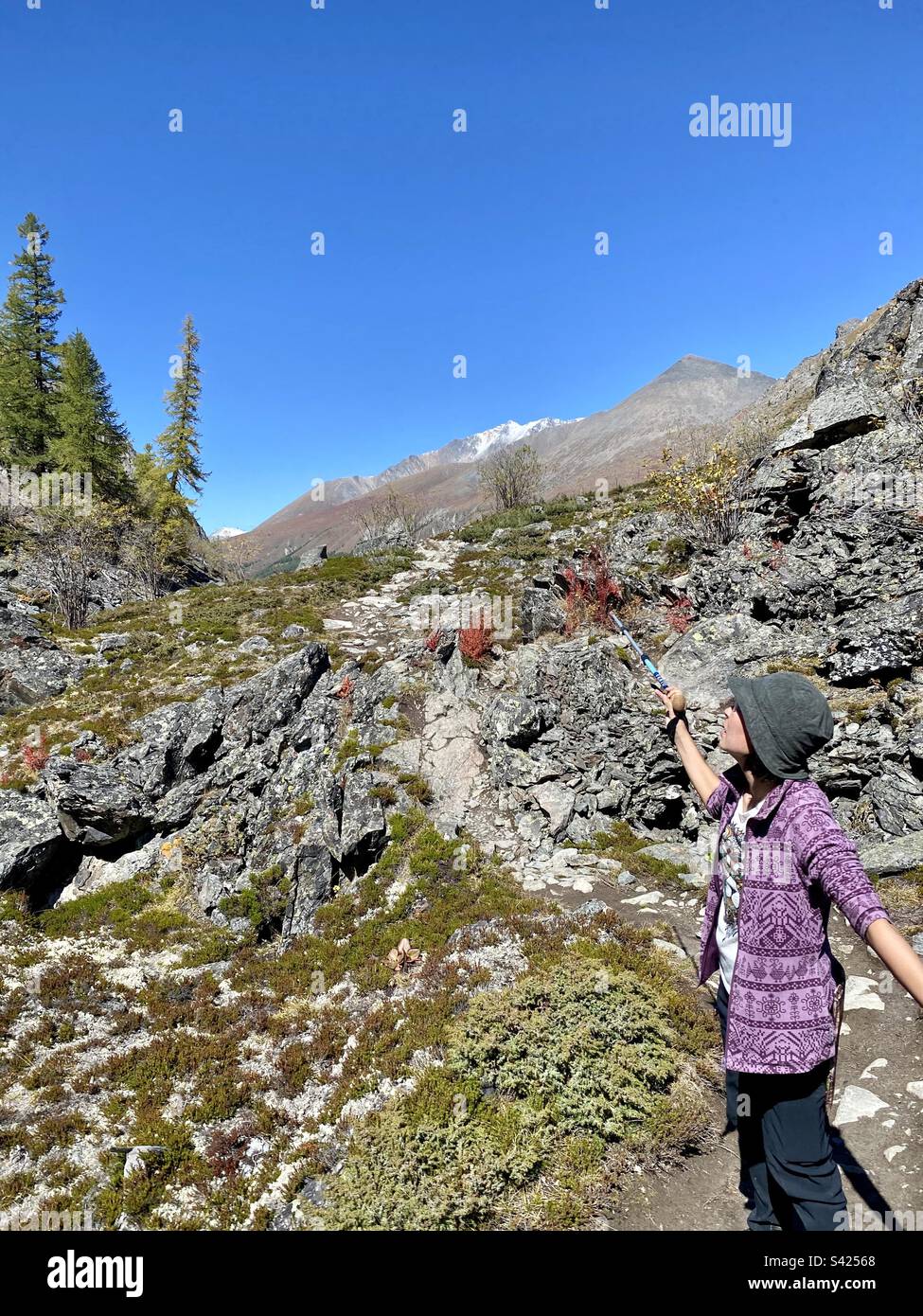 A traveler girl shows a tourist stick to a mountain in the Altai rocks in Siberia. - Smartphone Captured Stock Image