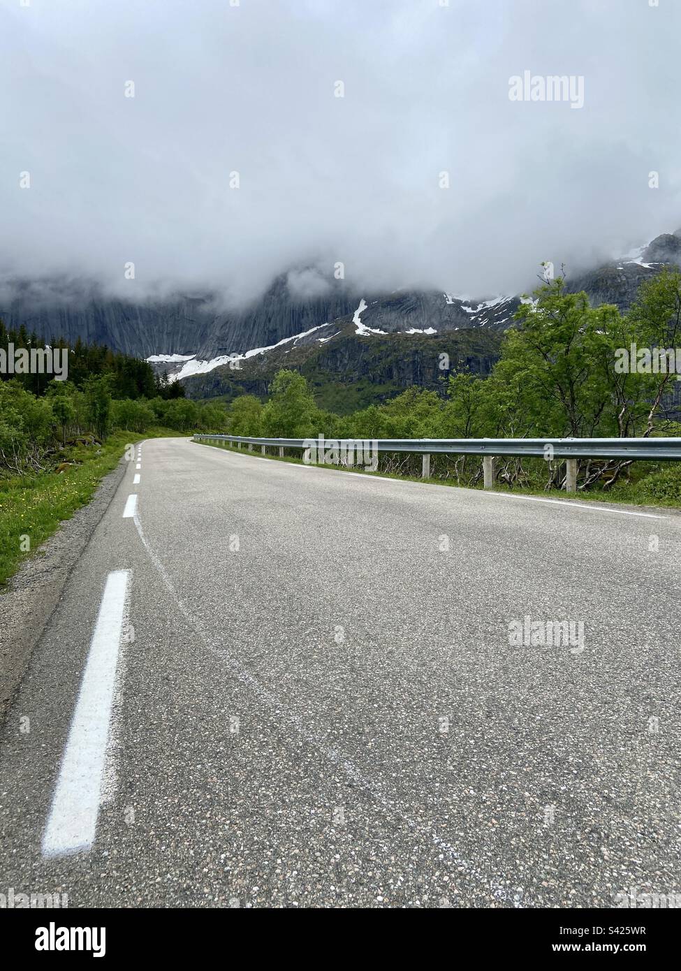 Road to town Nusfjord in Lofoten islands, Norway. You can see mountain Stjerntinden covered in clouds. Photo taken on a summer evening, low near asphalt road. - Smartphone Captured Stock Image