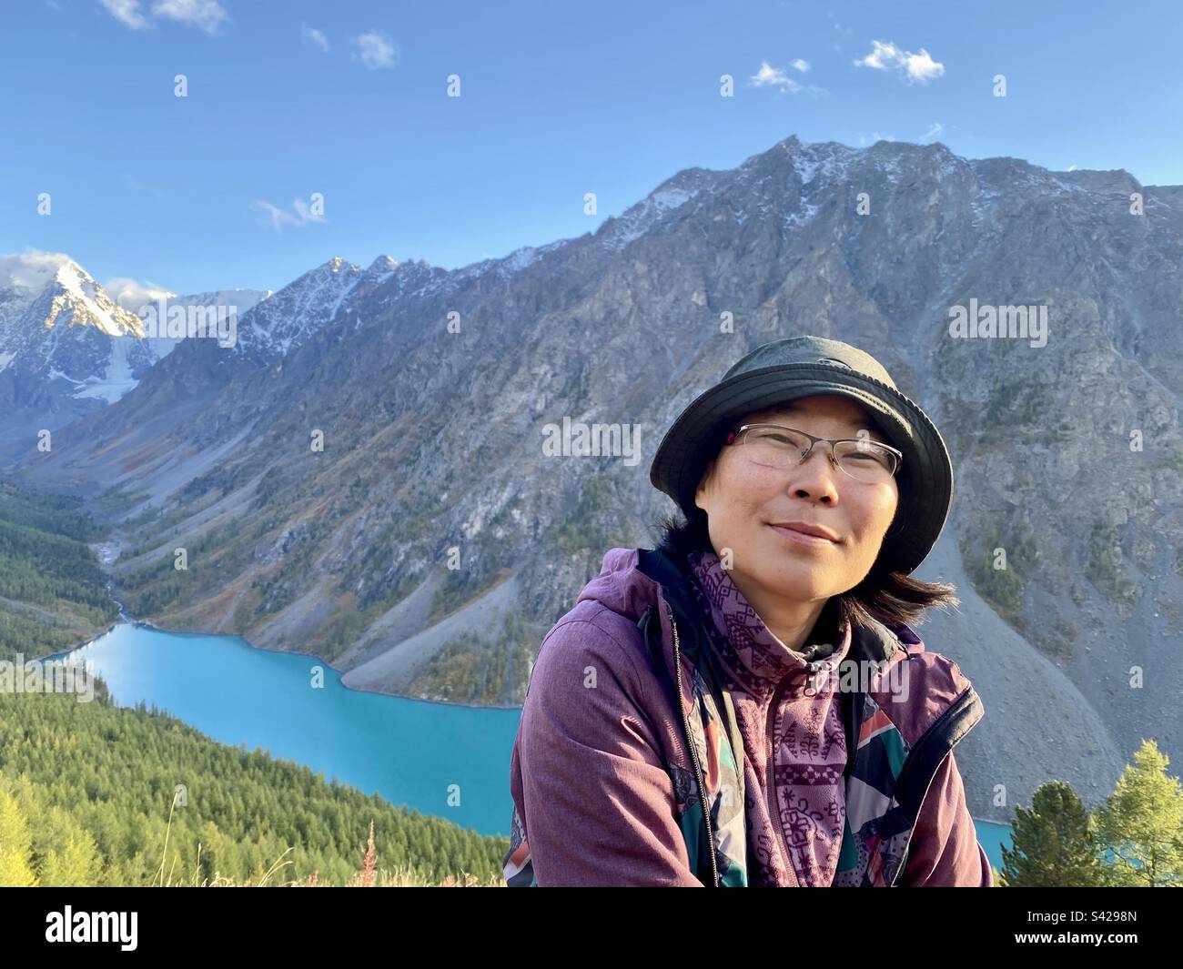 Portrait of a smiling Asian girl tourist Yakut on a rock near an Alpine lake at sunset in the Altai mountains. Stock Photo