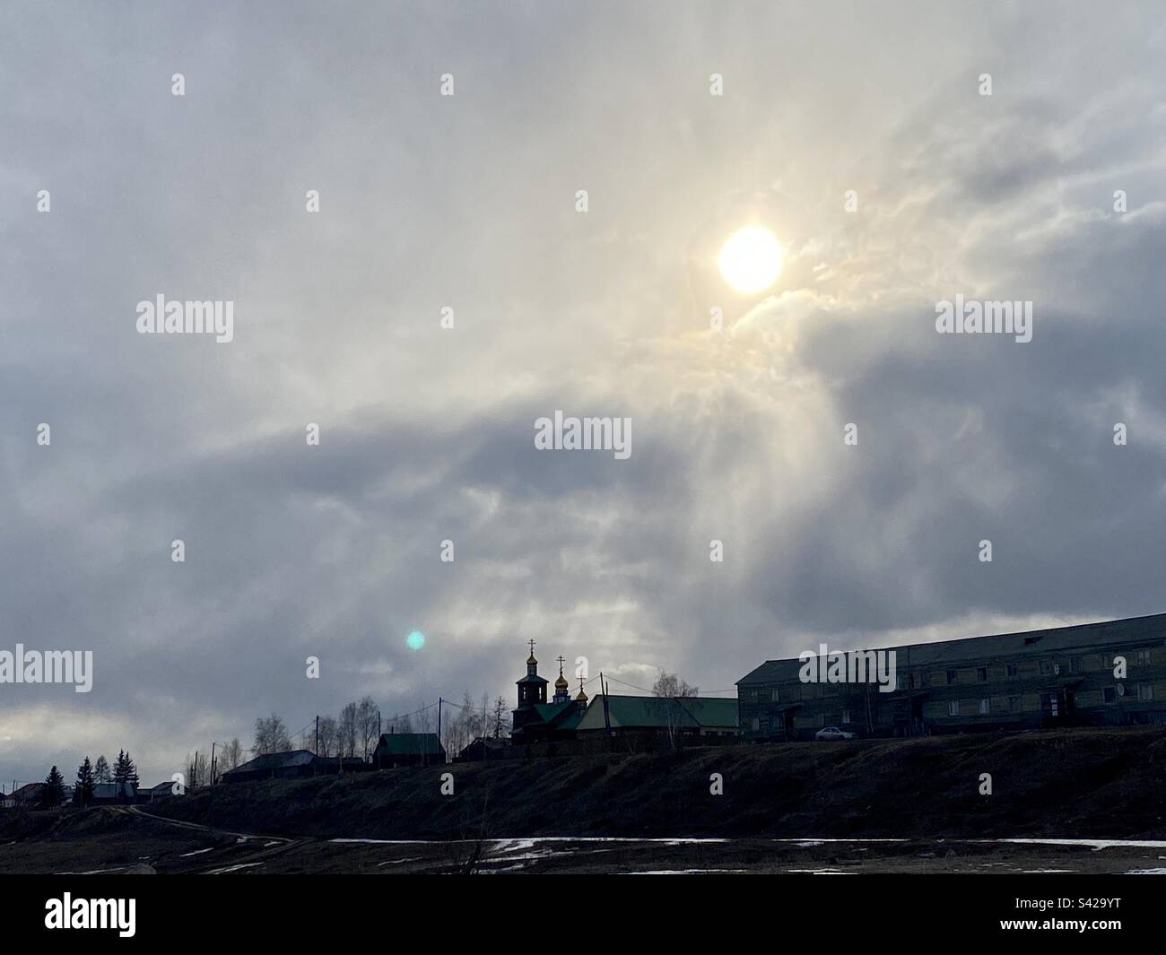 The sun shines rays through the clouds at the houses and domes of the church in the village of Yakutia in Suntar in Siberia. - Smartphone Captured Stock Image