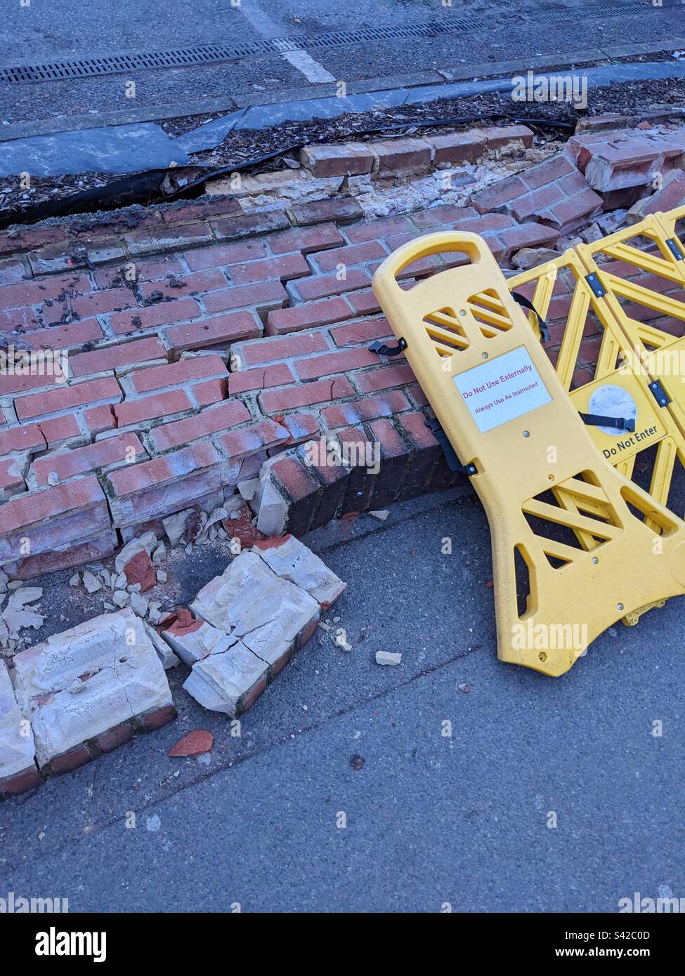 Broken fallen down wall hit by a car with yellow warning sign Stock