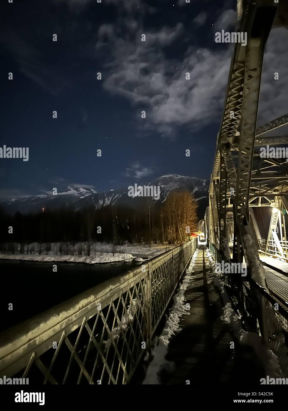 A one lane bridge in Revelstoke, BC leading straight to mount Begbie, with a starry night sky. Stock Photo