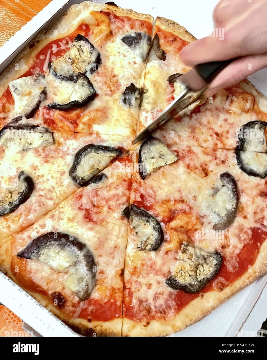 Human hand cutting pizza slices with pizza cutter at home in a box