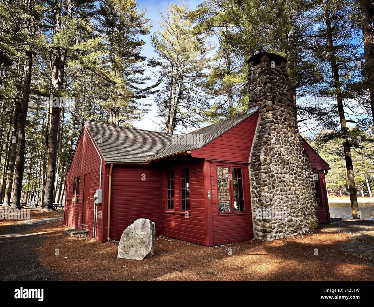 Red cabin with stone chimney surrounded by fir trees in Chatfield Hollow State Park in Killingworth, Connecticut, USA - Smartphone Captured Stock Image