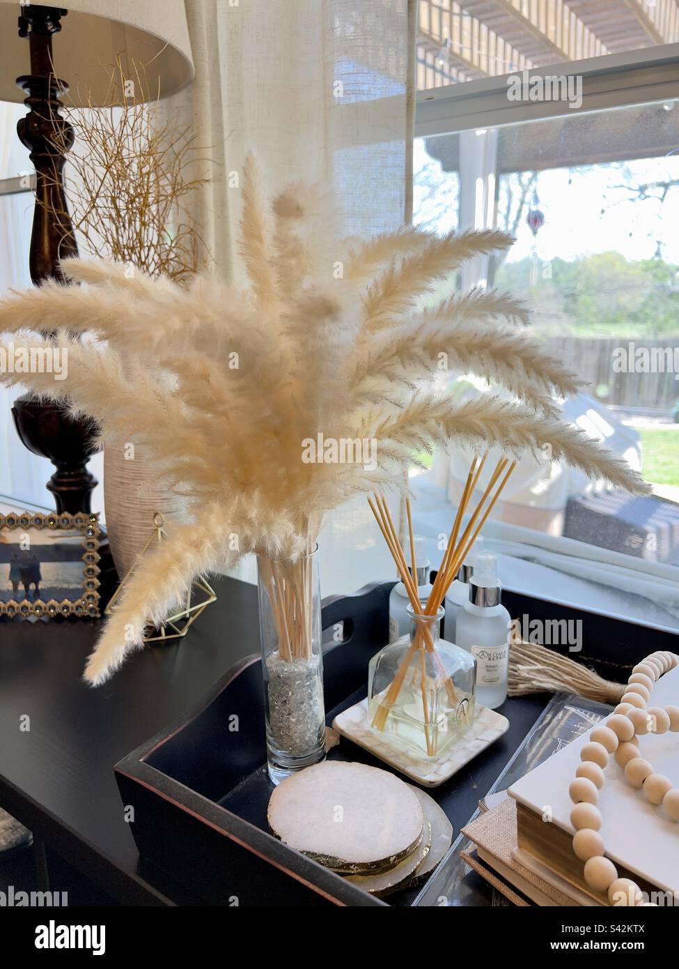 White feather plumes in a stem vase in front of a window part of home