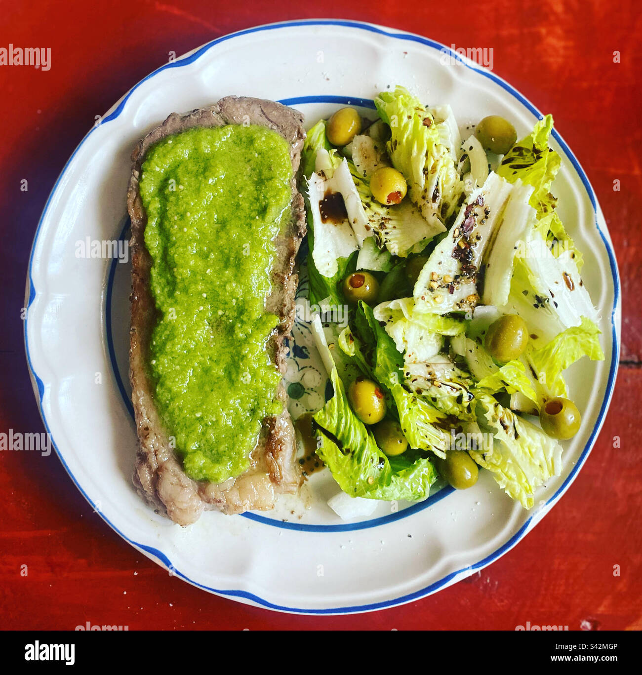 Meat covered with green sauce with sauce salad and olives in a home in