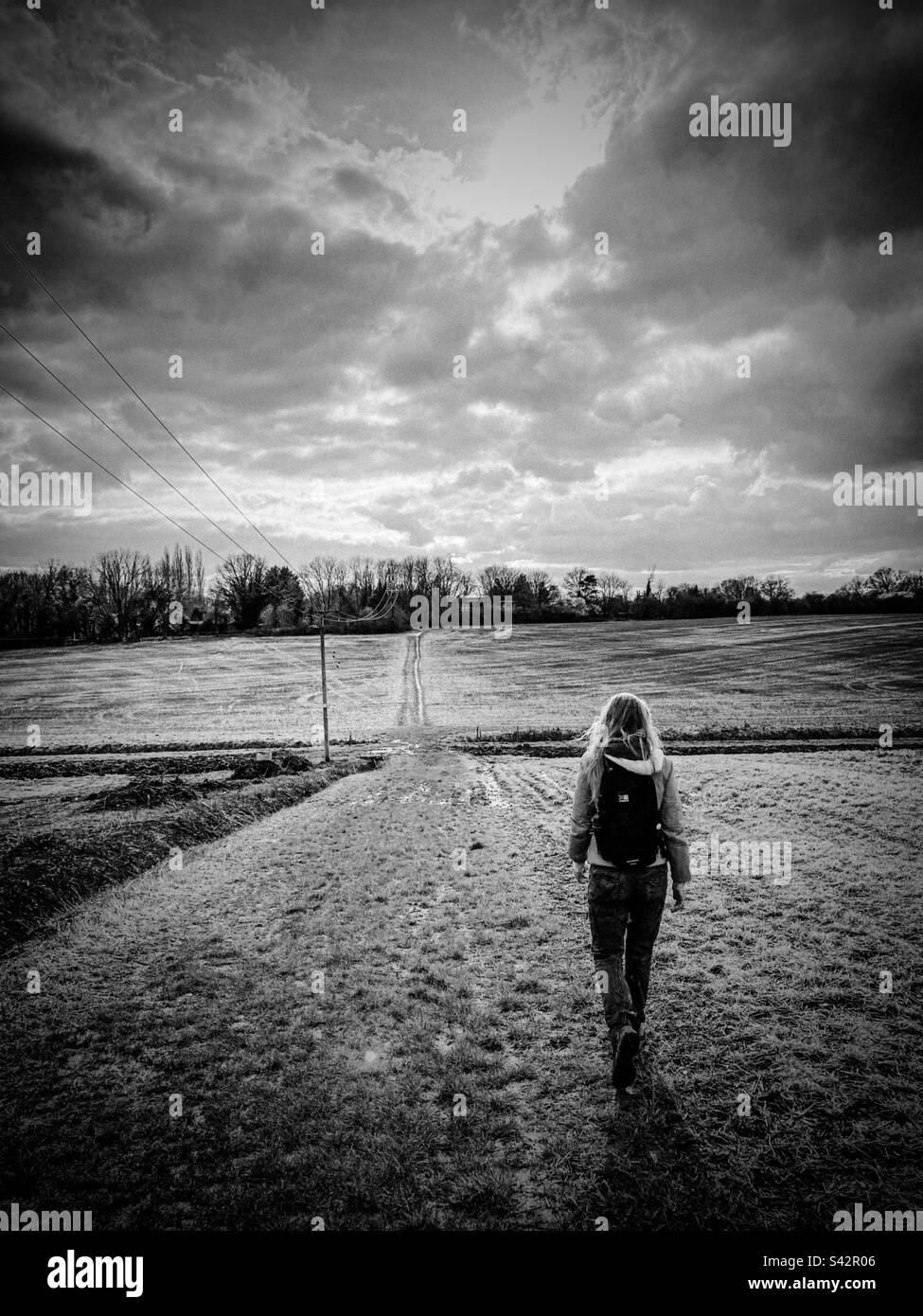 A woman with a backpack walks along a track in the countryside in England - Smartphone Captured Stock Image