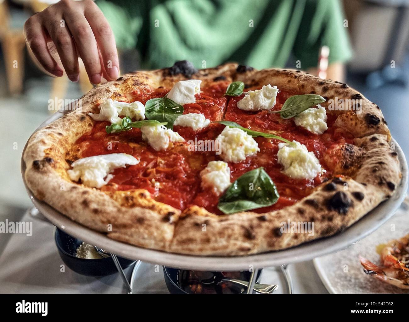 Human hand reaching out for bufalina pizza on plate on table. - Smartphone Captured Stock Image