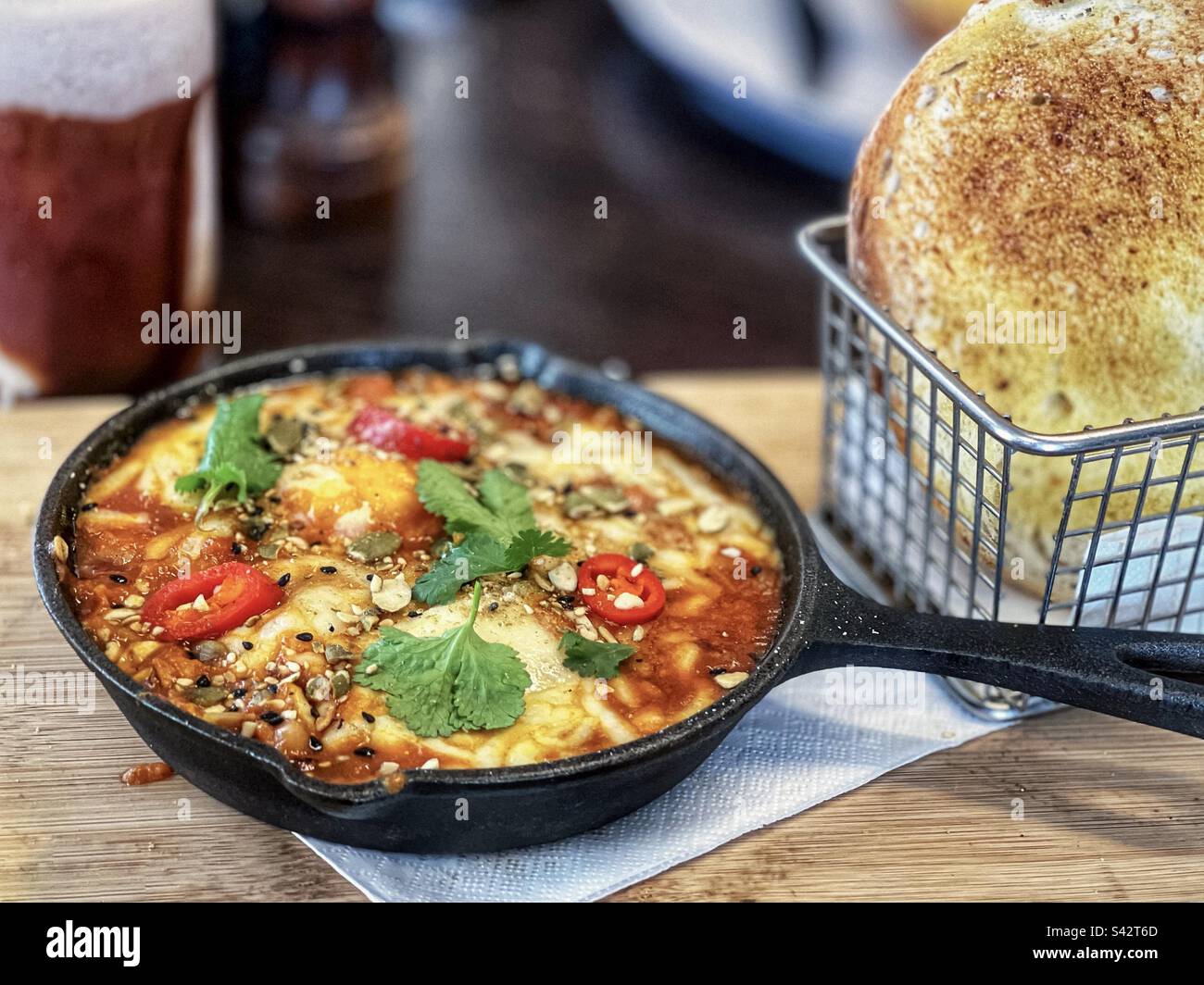 Shakshuka in skillet and sourdough bread on serving board on table. - Smartphone Captured Stock Image