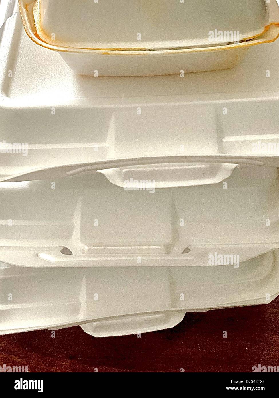 4 white styrofoam takeout leftovers containers stacked on wooden table - Smartphone Captured Stock Image
