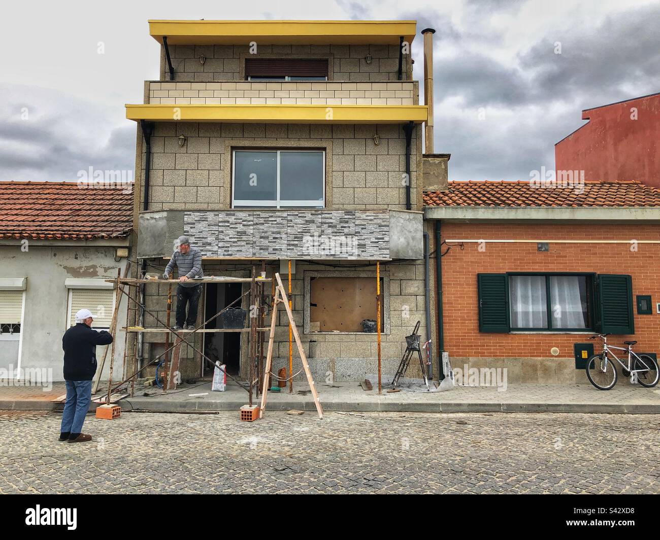 A man on the scaffolding talking to another man standing on the road in Espinho, Portugal, 2023 - Smartphone Captured Stock Image