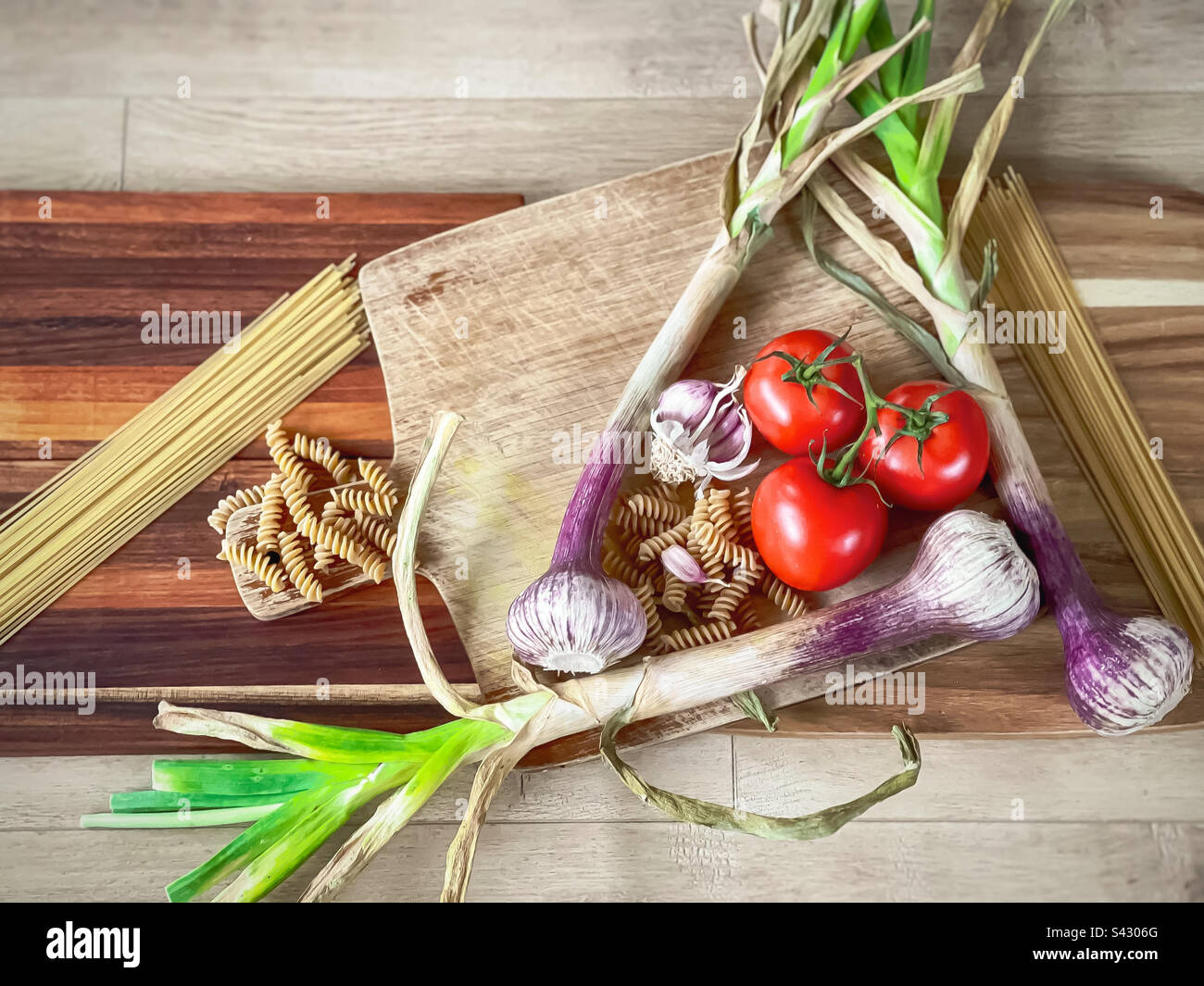 Directly above view of tomatoes, fresh garlic, spiral pasta and spaghetti arranged on wooden cutting boards on wood. - Smartphone Captured Stock Image