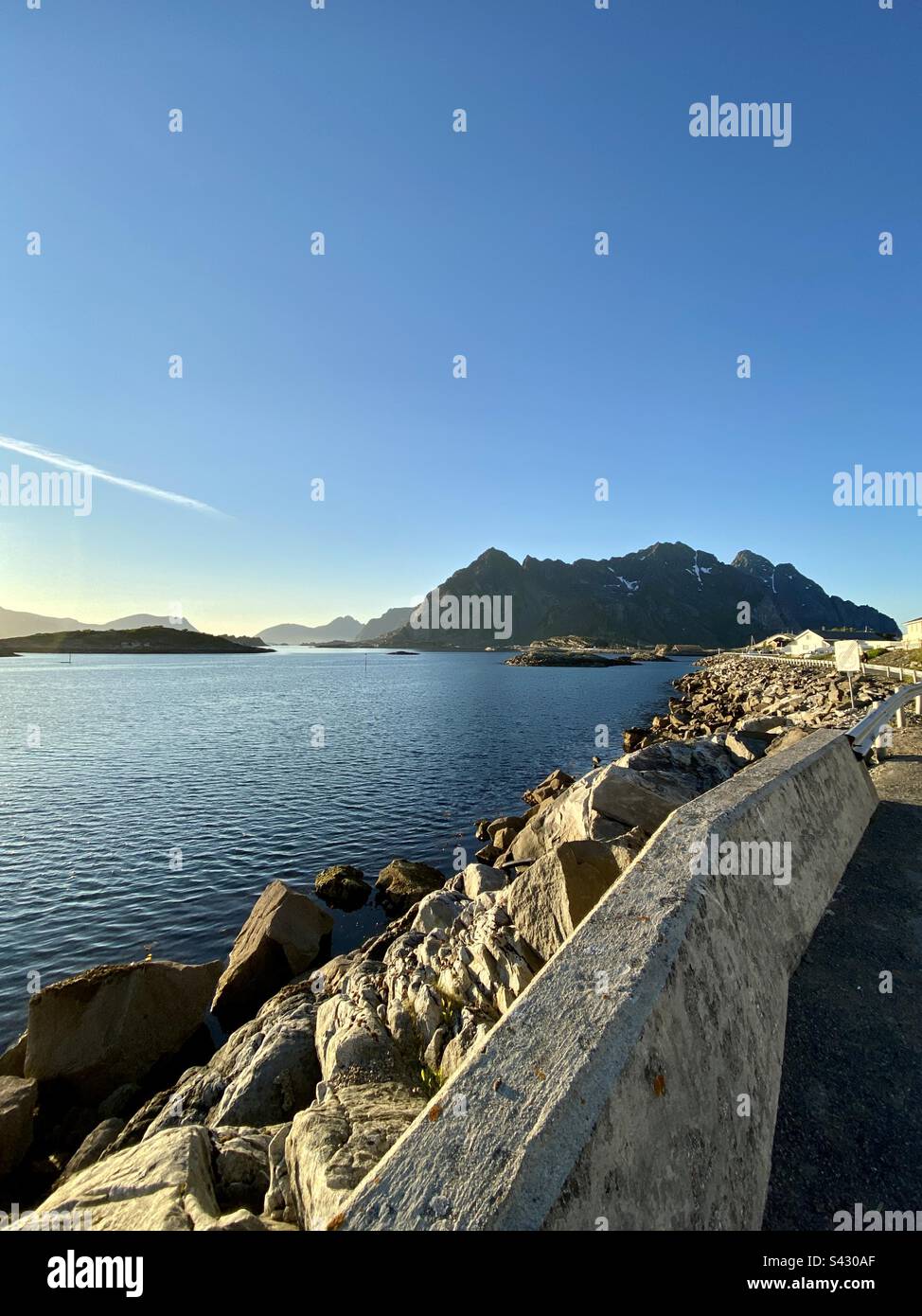 Roadside view in Henningsvær, Lofoten islands on a sunny late summer evening. Warm colours because of the evening sun and beautiful view in Lofoten islands to the mountains and some smaller islands. - Smartphone Captured Stock Image