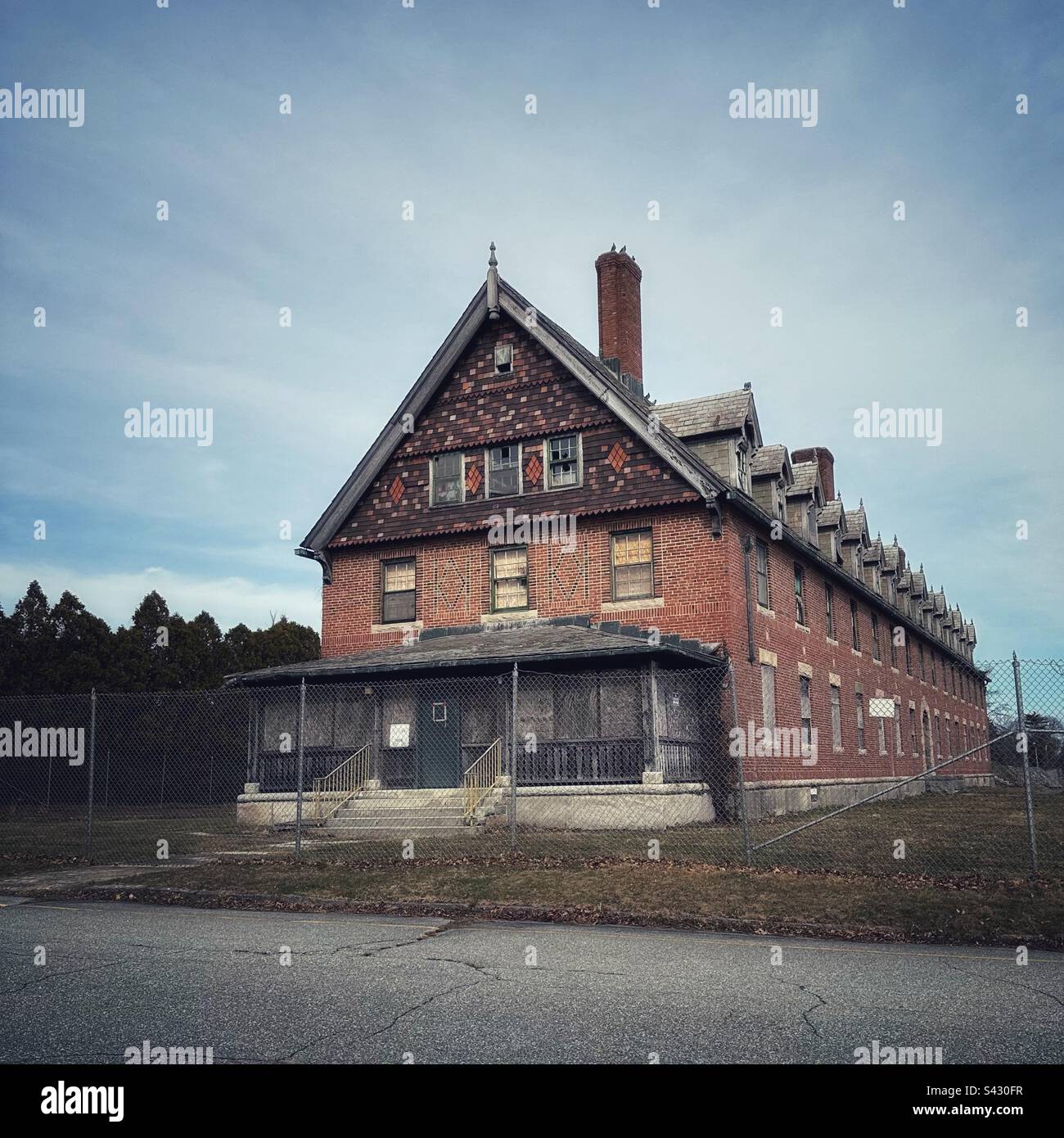 Grunge concept of abandoned medical facility in Waterford, Connecticut, USA. Road in the front with metal fence around red brick building. - Smartphone Captured Stock Image