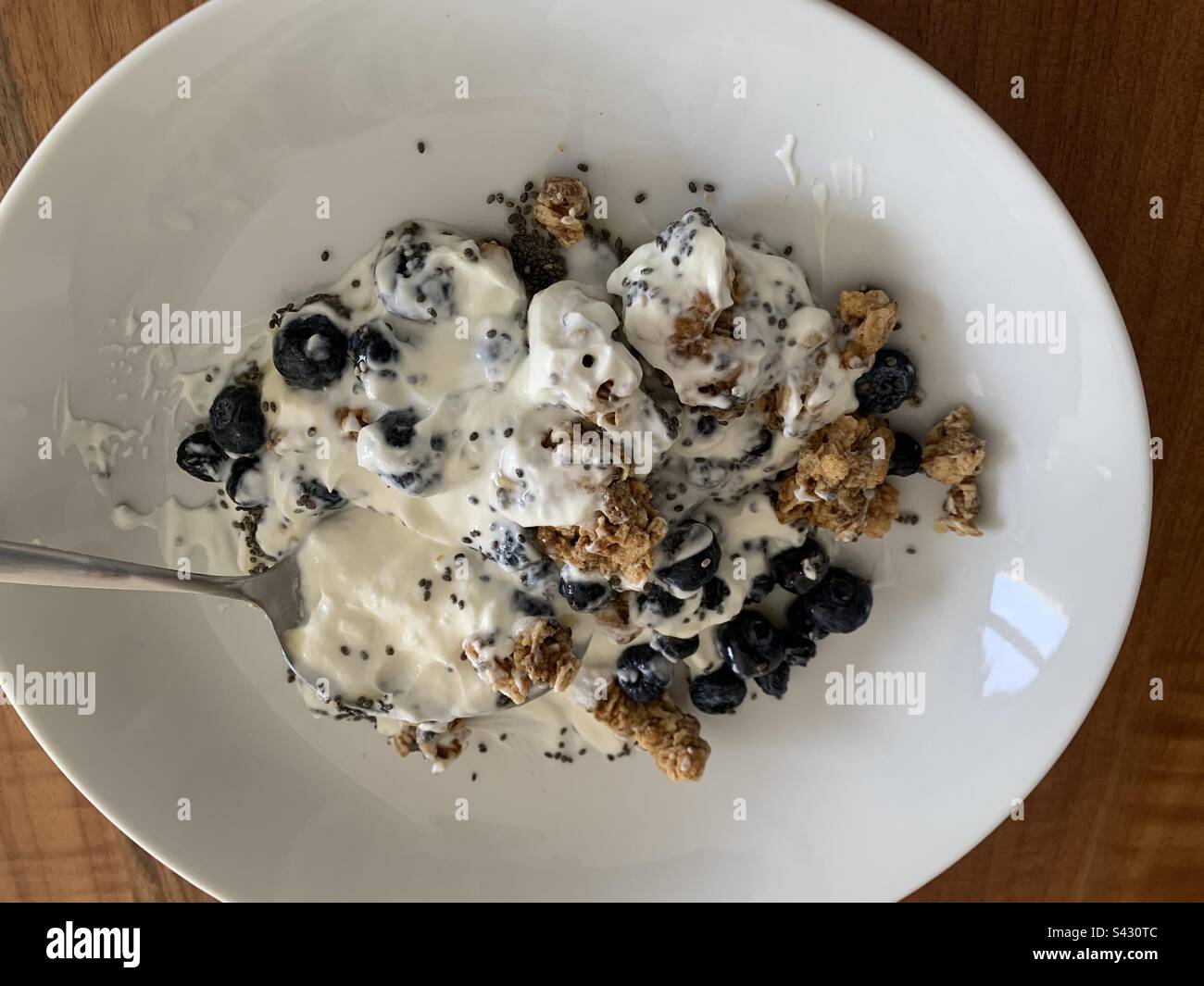 A bowl of Greek yoghurt with granola, blueberries, chia seeds and honey against a wooden background - Smartphone Captured Stock Image
