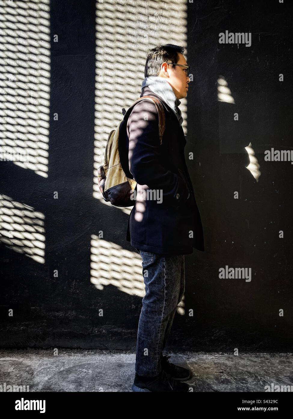 Full length shot of side view of young man standing against shadowed patterned wall. - Smartphone Captured Stock Image