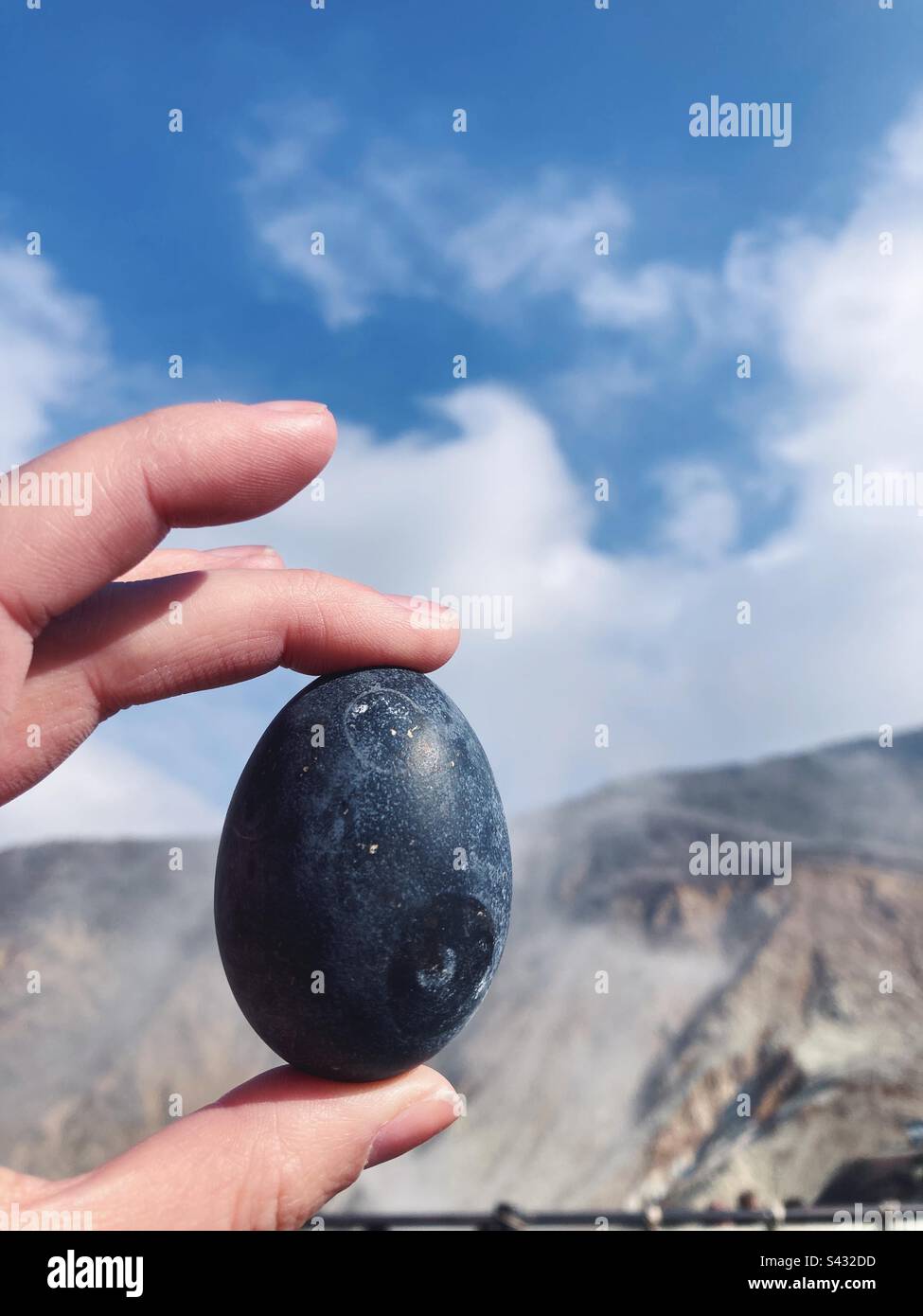 Hand holding a black egg, which has been boiled in Owakudani’s hot springs, with steam visible in the background. Halone, Japan. - Smartphone Captured Stock Image