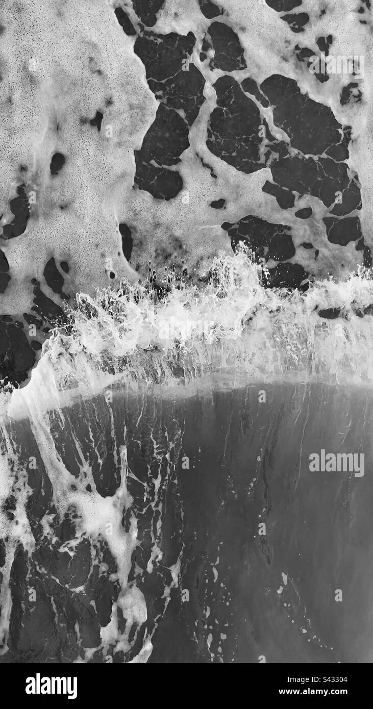 Monochrome overhead image of waves and receding water on shoreline sea Stock Photo